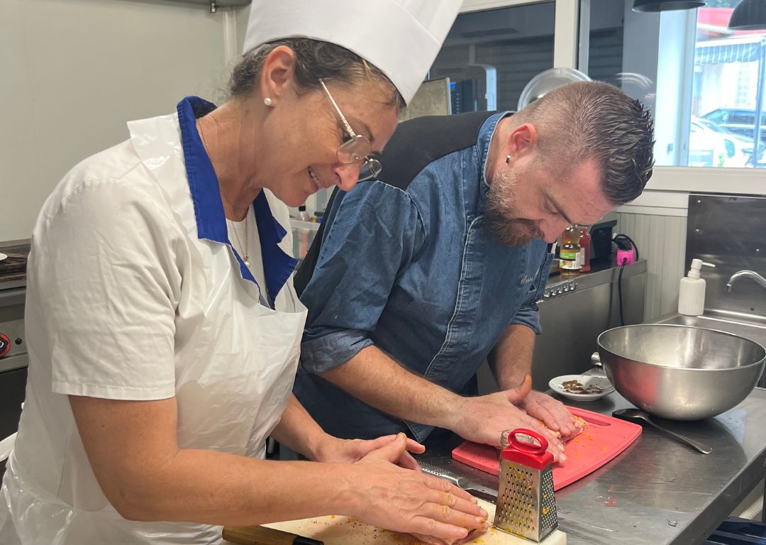 Formation en cuisine professionnelle - le formateur guide la participante dans la préparation d'ingrédients, en râpant et en coupant sur un plan de travail