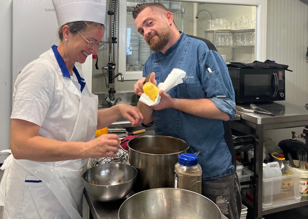 Photo réelle d'une de nos formations en bases de cuisine professionnelle. Le formateur explique à la participante comment préparer un ingrédient dans une cuisine professionnelle.